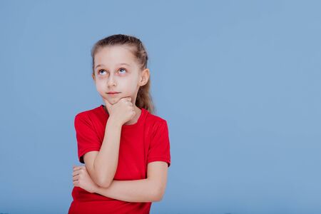 thinking child in red t-shirt touching chin and looks up isolated on blue backgroundの写真素材