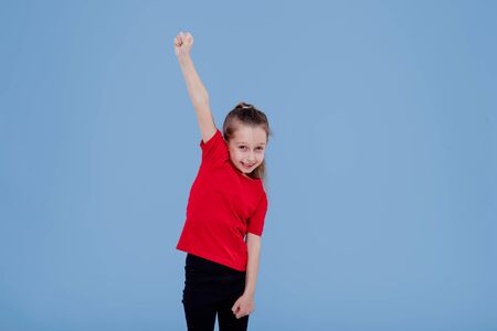 happy little girl in casual outfit celebrating achievement with raised arm while isolated on blue backgroundの写真素材