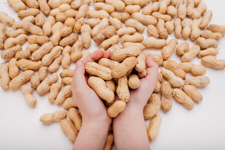 From above of pile of unpeeled peanuts in hands of crop anonymous person and on white tableの写真素材