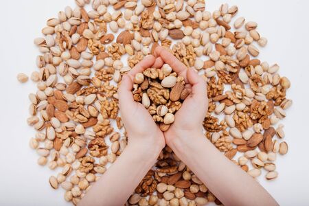 two hands of a child with assortment of nuts. walnut, pistachio, almonds, hazelnuts, on white background, top viewの写真素材