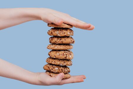 a child's hand with oat biscuits with seeds isolated on blue background, in studioの写真素材