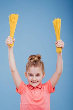 RAW Spaghetti held in the hand of a child, solated on blue backgroundの写真素材