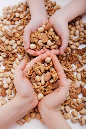 Group of nuts in the four hands of a child. walnut, pistachio, almonds, hazelnuts, on white background, top viewの写真素材