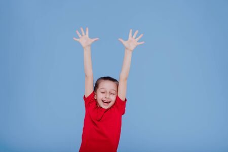 happy child in red outfit raising arms and jumping while having fun and celebrating success in studio isolated on blue backgroundの写真素材