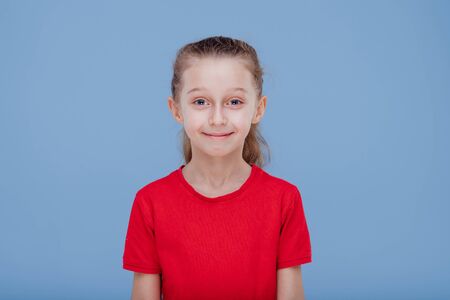 Funny surprised little girl in red t shirt staring at camera dressed in red T-shirt, isolated on blue background, in studioの写真素材