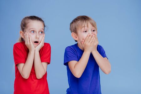 two scared children with hands on face isolated on blue background, in studioの写真素材