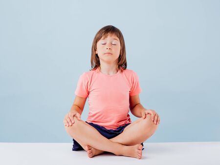 little girl practicing yoga, isolated on blue background, copy space, in studioの写真素材