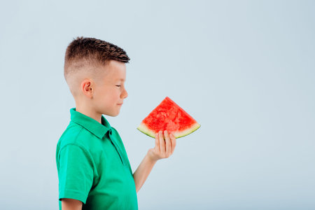 little boy with slice of watermelon in hand. isolated on blue background, copy space, in studio, profile viewの写真素材