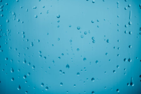 Water drops on blue glass covering smooth surface of transparent blue glass