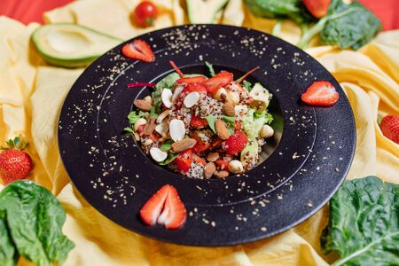 High angle of plate of yummy vegetarian salad with ripe strawberries placed on yellow clothの写真素材