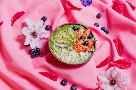 Top view of bowls with sweet fruit dishes placed on pink cloth amidst fresh flowersの写真素材