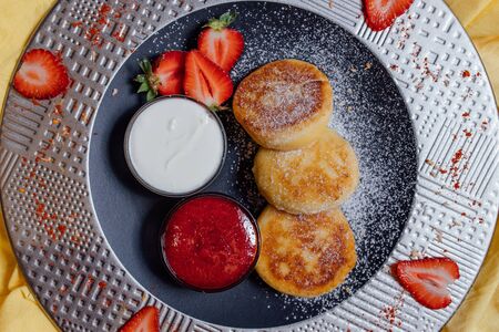 Top view of delicious dessert served on plate with bowls of strawberry jam and yoghurtの写真素材