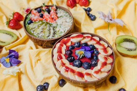 Top view of bowls with sweet fruit dishes placed on yellow cloth amidst fresh flowersの写真素材