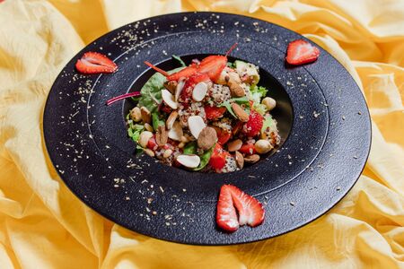 High angle of plate of yummy vegetarian salad with ripe strawberries placed on yellow clothの写真素材