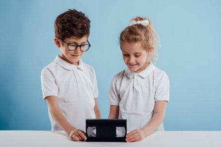 two smiling childs with video tape, isolated on blue background, old gadgetsの写真素材