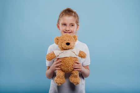 happy little girl with bear toy isolated on blue background, studio shotの写真素材