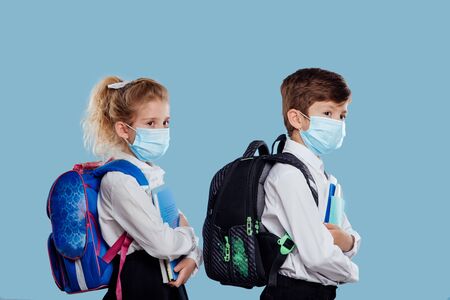 Side view of classmates in sterile blue masks with backpacks and textbooks standing on blueの写真素材