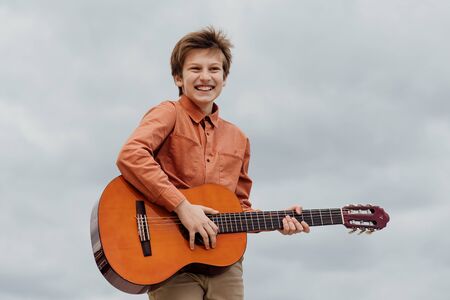 excited boy plays guitar, dressed in a shirt, sky in the backgroundの写真素材