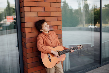 preteen with guitar, leaning against the brick wall dressed in a shirt, wall in background