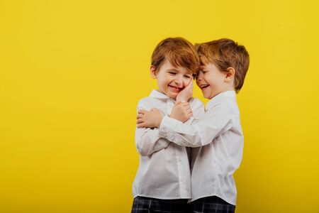 two little boys are hugging, playing, dressed in white shirt and jeans, isolated on a yellow background, studio shotの写真素材
