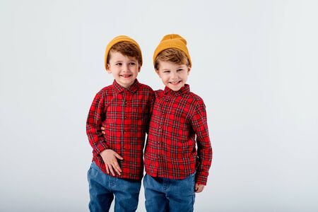 two handsome little brothers hug, dressed in red shirt with squares and jeans, isolated on white background, studio shotの写真素材