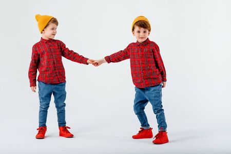 two happy little children play and hold hands, dressed in red shirt with squares and jeans, isolated on white background, studio shotの写真素材