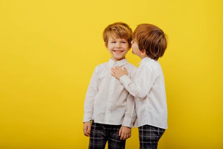 two little boys are hugging, playing, dressed in white shirt and jeans, isolated on a yellow background, studio shotの写真素材