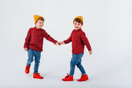 two happy little boys are playing in studio, dressed in red shirt with squares and jeans, isolated on white background, studio shotの写真素材