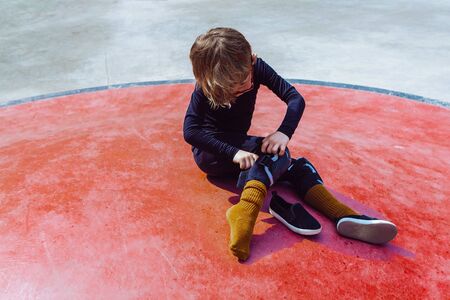 High angle of boy adjusting protective gear on knee while sitting on cement ground in skate parkの写真素材