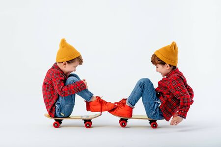 two children are sitting on a skateboard and playing, dressed in red shirt with squares and jeans, isolated on white background, studio shotの写真素材