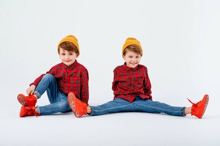 two little boys with legs apart, looking at camera, dressed in red shirt with squares and jeans, isolated on white background, studio shotの写真素材