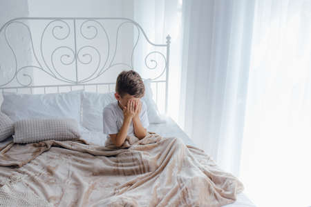 little boy wipes his eyes, he is in bed, the child wakes up in the morningの写真素材