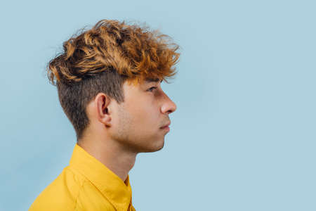profile view, teenager with fashionable hairstyle, handsome guy in yellow shirt, young guy, attractive teenager, blue background, studio shotの写真素材