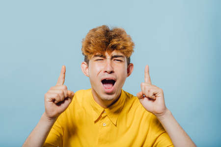 Wow, look up! Portrait of amazed boy pointing up to empty place on blue background, expressing shock surprise with wide open mouth and showing copy space for advertisement. indoor studio shotの写真素材