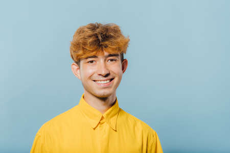 Portrait of a handsome teenage boy, young guy, attractive young man, teenager with fashionable hairstyle, blue background, studio shotの写真素材