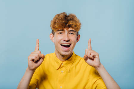 Portrait of a happy boy pointing fingers up at copy space isolated over blue backgroundの写真素材