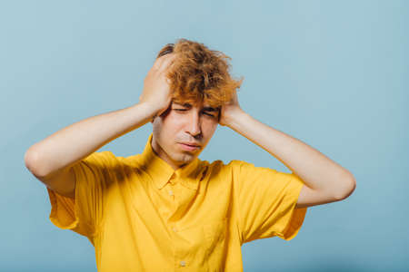 teenager in depression, who has problems in yellow shirt, young guy, attractive young man, teenager with fashionable hairstyle, blue background, studio shotの写真素材