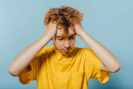 teenager who has problems in yellow shirt, young guy, attractive young man, teenager with fashionable hairstyle, blue background, studio shotの写真素材