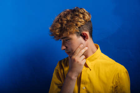 handsome young man in yellow shirt, young guy, attractive young man, teenager with fashionable hairstyle, blue background, studio shotの写真素材