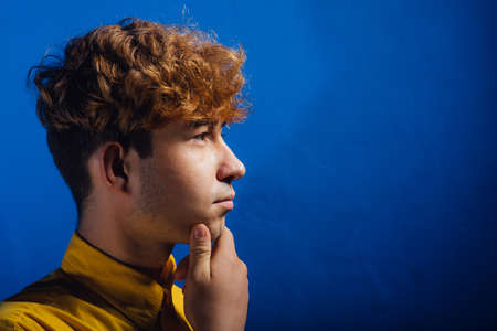 profile view of handsome young man in yellow shirt, young guy, attractive teenager, teenager with fashionable hairstyle, blue background, studio shotの写真素材