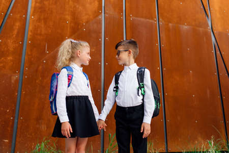 little schoolchildren look at each other. two schoolchildren, a boy and a girl, hold handsの写真素材