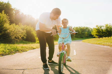 Dad is teaching daughter how to ride bicycle the street, Child learning to ride a bike. Family activities at summer.の写真素材