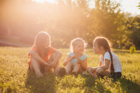 Three adorable little girls play together in a garden, outdoors, happy childhood. children sitting on the green grassの写真素材