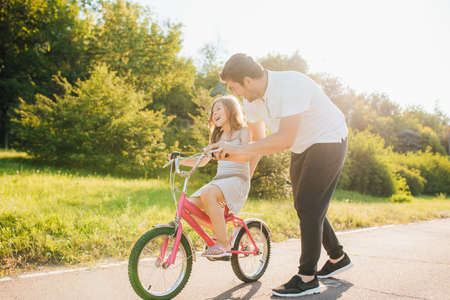 Young father teaching his daughter to ride bicycle outdoors, on the streetの写真素材