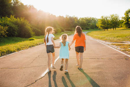 back view, three little girls walk on the street, holding hands, sunny day, outdoorsの写真素材