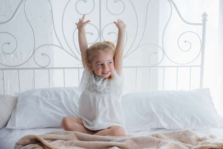 morning awakening child girl in bed, smiling little caucasian child it feels good in cozy bedroom in the morning at homeの写真素材
