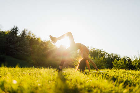Young woman doing yoga in morning park. Young female exercising vital fitness at outdoors nature with trees background.の写真素材
