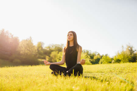 woman meditates sitting on the grass, doing yoga at sunsetの写真素材
