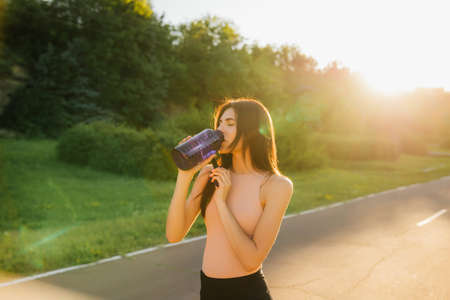 Sporty woman drinking water outdoor at sunset. girl drinking water after a good exerciseの写真素材