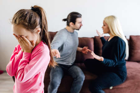 caucasian kid little girl upset stressed children close face, suffering from negative emotions, blurred parents shouting, arguing with each other on background, family problem, break up, divorce concept.の写真素材